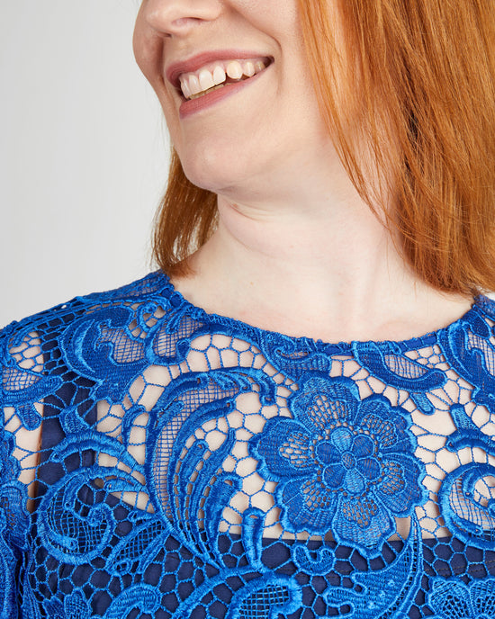 Close-up of a person wearing a blue lace dress with a plain background. This top is the Montrose Top sewing pattern from Cashmerette.