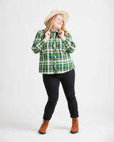 Woman wearing a green plaid shirt, black pants, and brown boots on a white background. This top is the Vernon Shirt sewing pattern from Cashmerette.