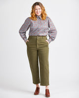 Woman wearing a floral blouse and green pants on a white background. This top is the Vernon Shirt sewing pattern from Cashmerette.
