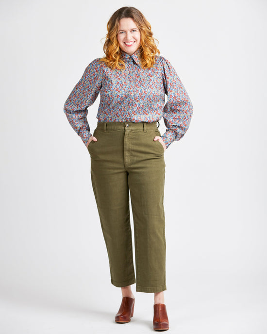Woman wearing a floral blouse and green pants on a white background. This top is the Vernon Shirt sewing pattern from Cashmerette.