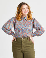Woman wearing a floral blouse and green pants against a plain background. This top is the Vernon Shirt sewing pattern from Cashmerette.