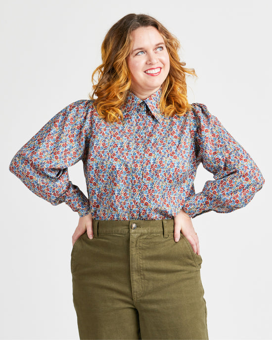 Woman wearing a floral blouse and green pants against a plain background. This top is the Vernon Shirt sewing pattern from Cashmerette.