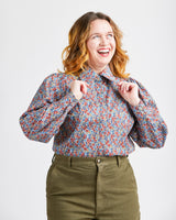 Woman wearing a floral blouse and green pants on a white background. This top is the Vernon Shirt sewing pattern from Cashmerette.