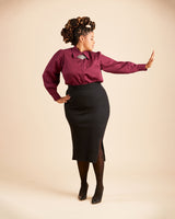 Woman wearing a burgundy blouse and black skirt against a beige background. This top is the Vernon Shirt sewing pattern from Cashmerette.