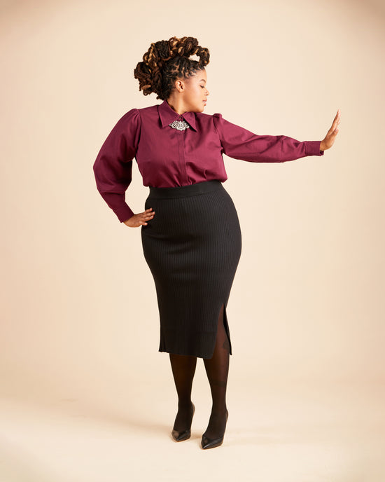 Woman wearing a burgundy blouse and black skirt against a beige background. This top is the Vernon Shirt sewing pattern from Cashmerette.