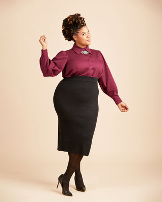 Woman wearing a burgundy blouse and black skirt on a beige background. This top is the Vernon Shirt sewing pattern from Cashmerette.