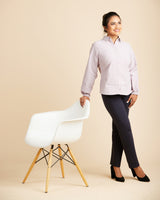 Woman in a light purple shirt and dark pants standing next to a white chair on a beige background. This top is the Vernon Shirt sewing pattern from Cashmerette.