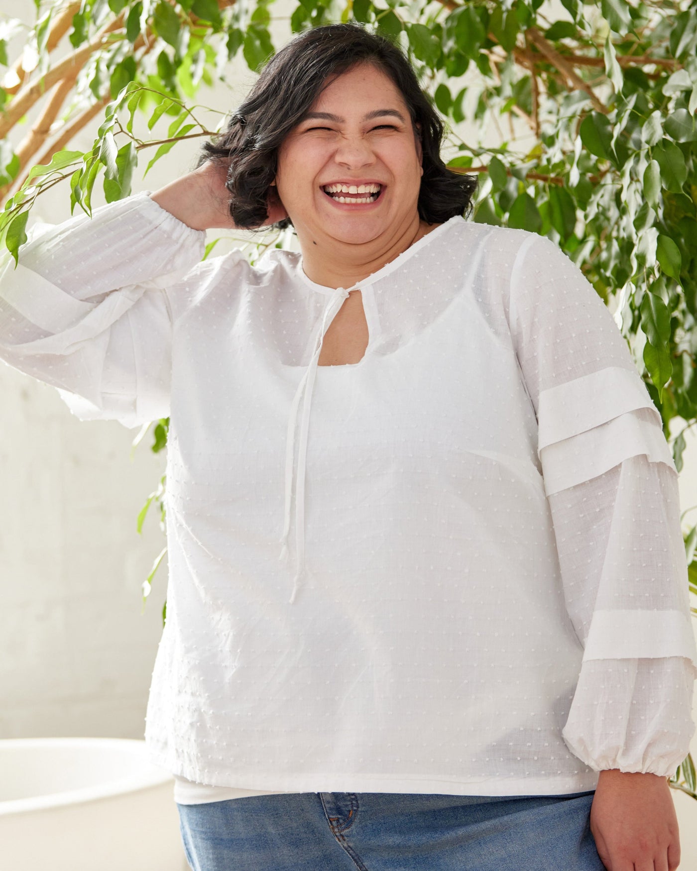 Person wearing a white blouse with sheer sleeves in front of a plant. This top is the Alton Blouse sewing pattern from Cashmerette.