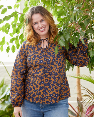 Woman wearing a patterned blouse and jeans standing among green foliage. This top is the Alton Blouse sewing pattern from Cashmerette.