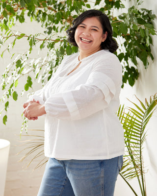 Woman wearing a white blouse and blue jeans standing among green plants. This top is the Alton Blouse sewing pattern from Cashmerette.