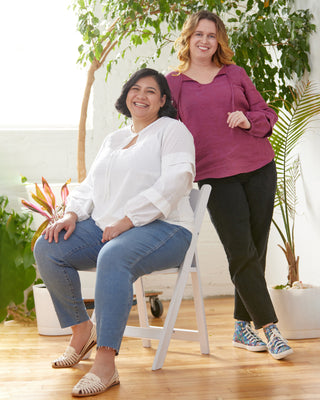 Two women sitting together in a bright room with plants. This top is the Alton Blouse sewing pattern from Cashmerette.