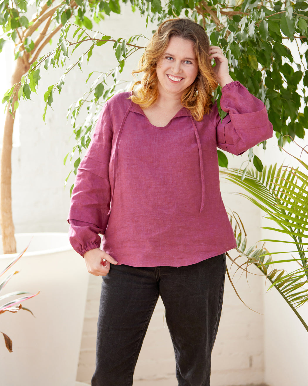 Woman wearing a pink blouse standing in front of green plants. This top is the Alton Blouse sewing pattern from Cashmerette.