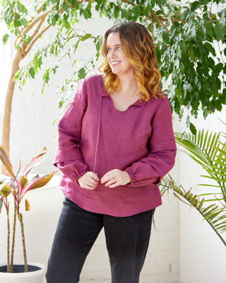 Woman wearing a magenta blouse standing among green plants indoors. This top is the Alton Blouse sewing pattern from Cashmerette.