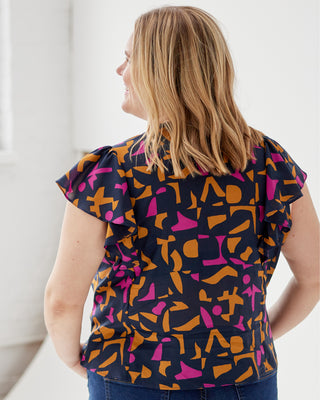 Woman wearing a colorful patterned top with ruffled sleeves against a white background. This top is the Selwyn Top sewing pattern from Cashmerette.