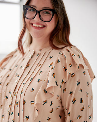 Woman wearing a beige blouse with a pattern, smiling against a white background. This top is the Selwyn Top sewing pattern from Cashmerette.