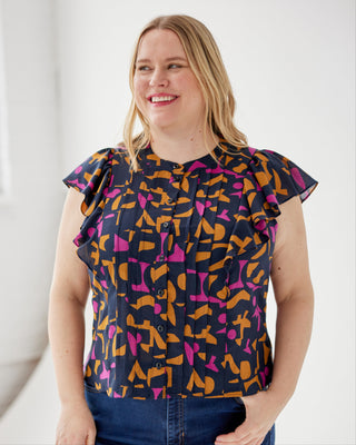 Woman wearing a colorful patterned blouse with ruffled sleeves against a white background. This top is the Selwyn Top sewing pattern from Cashmerette.