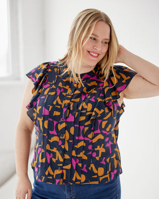 Woman wearing a colorful patterned top with a plain background. This top is the Selwyn Top sewing pattern from Cashmerette.