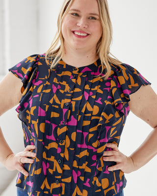 Woman wearing a colorful patterned blouse with a plain background. This top is the Selwyn Top sewing pattern from Cashmerette.