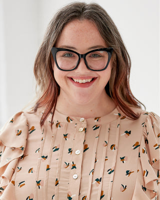 Woman wearing glasses and a patterned blouse against a plain background. This top is the Selwyn Top sewing pattern from Cashmerette.