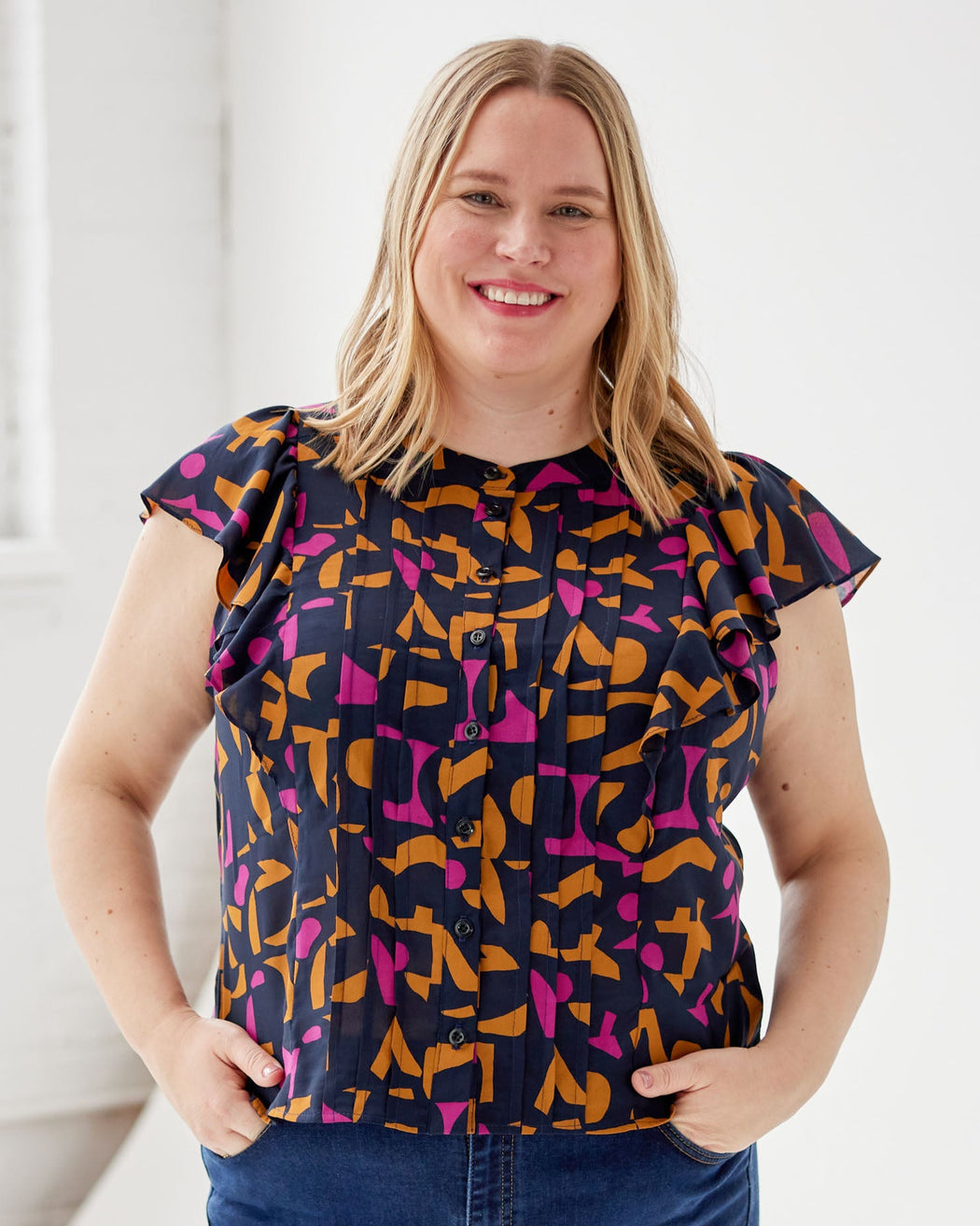 Woman wearing a colorful patterned blouse in a bright room. This top is the Selwyn Top sewing pattern from Cashmerette.