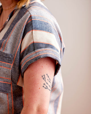 Person wearing a striped garment with a tattoo on their arm against a neutral background. Woman wearing a plaid shirt and denim shorts against a neutral background. This top is the Haskell Shirt sewing pattern from Cashmerette.