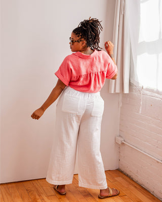 Person wearing a pink top and white pants standing in a room with wooden flooring and a window. Woman wearing a plaid shirt and denim shorts against a neutral background. This top is the Haskell Shirt sewing pattern from Cashmerette.