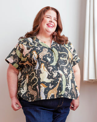 Woman wearing a patterned shirt with animal designs against a neutral background. Woman wearing a plaid shirt and denim shorts against a neutral background. This top is the Haskell Shirt sewing pattern from Cashmerette.