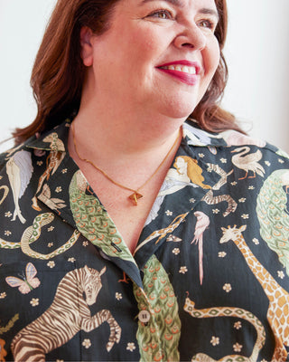 Woman wearing a patterned shirt with animals and nature designs. Woman wearing a plaid shirt and denim shorts against a neutral background. This top is the Haskell Shirt sewing pattern from Cashmerette.