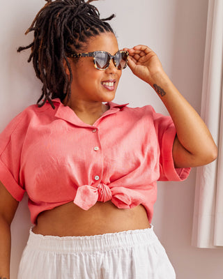 Woman wearing a pink cropped top and white pants, adjusting sunglasses against a neutral background. Woman wearing a plaid shirt and denim shorts against a neutral background. This top is the Haskell Shirt sewing pattern from Cashmerette.