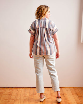 Person wearing a striped shirt and light-colored pants standing on a wooden floor with a white wall background. Woman wearing a plaid shirt and denim shorts against a neutral background. This top is the Haskell Shirt sewing pattern from Cashmerette.