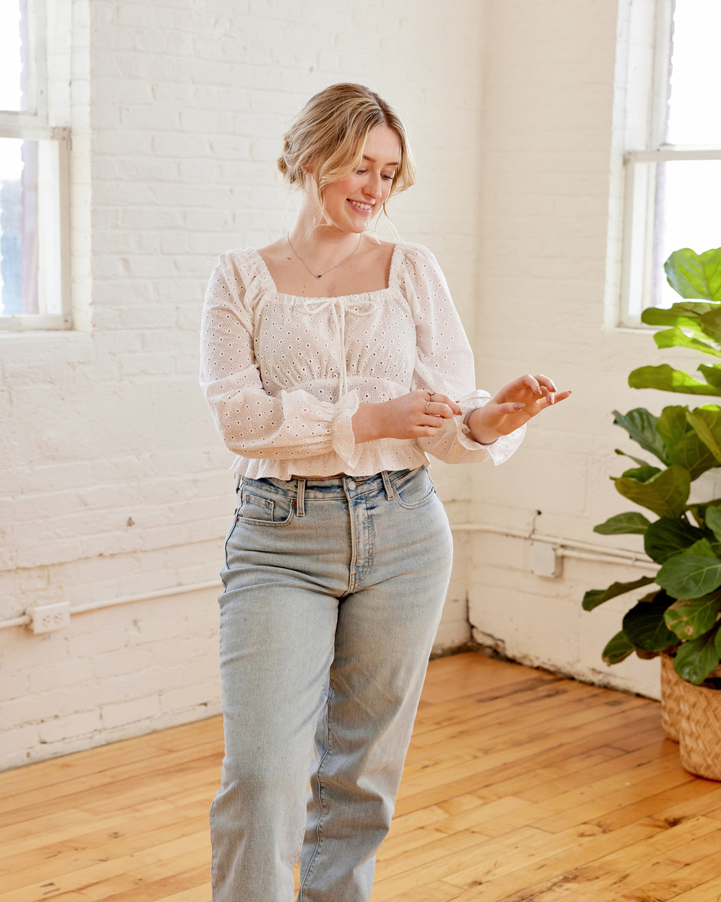 Woman in a light blouse and jeans standing in a room with white walls and wooden floor. This top is the Briarwood Top sewing pattern from Cashmerette.