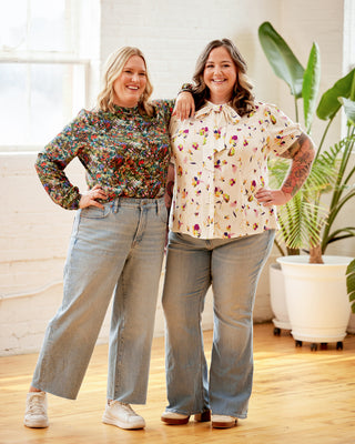 Two women standing together in a bright room with plants. This top is the Swanton Pussy Bow Blouse sewing pattern from Cashmerette.