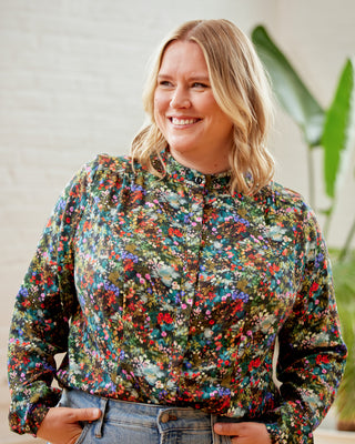 Person wearing a colorful floral blouse with a plant in the background. This top is the Swanton Pussy Bow Blouse sewing pattern from Cashmerette.