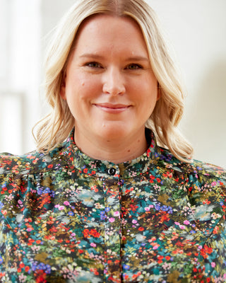 Woman wearing a colorful floral jacket with a blurred background. This top is the Swanton Pussy Bow Blouse sewing pattern from Cashmerette.