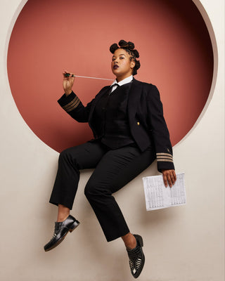 Person in a black suit sitting against a red circular wall. This vest is the Hartwell Vest sewing pattern from Cashmerette.