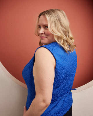 Woman wearing a blue sleeveless top against a red background. This vest is the Hartwell Vest sewing pattern from Cashmerette.