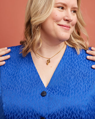 Person wearing a blue patterned top with a plain background. This vest is the Hartwell Vest sewing pattern from Cashmerette.