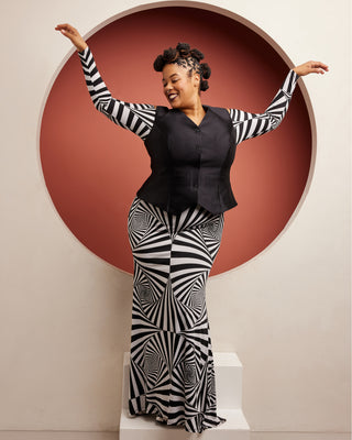 Person wearing a black and white striped outfit with a geometric pattern against a red circular backdrop. This vest is the Hartwell Vest sewing pattern from Cashmerette.