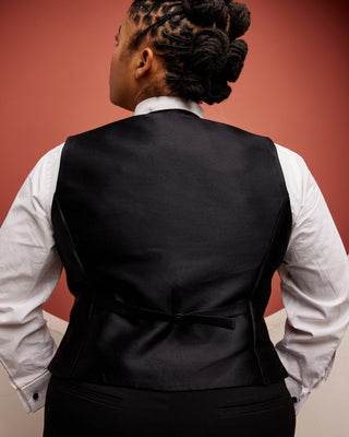 Person wearing a black vest over a white shirt against a red background. This vest is the Hartwell Vest sewing pattern from Cashmerette.