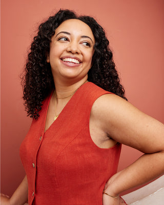 Woman wearing a red sleeveless top against a pink background. This vest is the Hartwell Vest sewing pattern from Cashmerette.