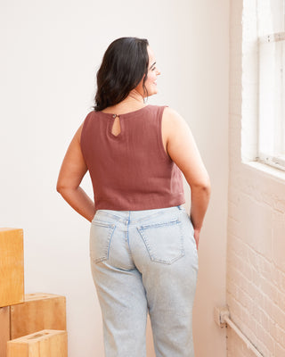 Woman wearing a brown sleeveless top and light blue jeans standing in a room with wooden blocks. This top is the Thorndike Tank sewing pattern from Cashmerette.