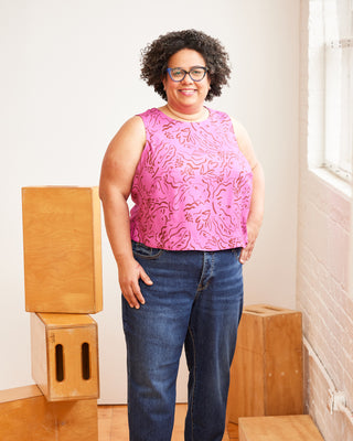 Woman wearing a pink sleeveless top and blue jeans standing indoors. This top is the Thorndike Tank sewing pattern from Cashmerette.