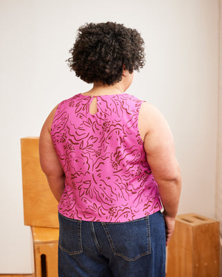 Person wearing a pink sleeveless top with floral pattern and blue jeans, standing in a room with wooden furniture. This top is the Thorndike Tank sewing pattern from Cashmerette.
