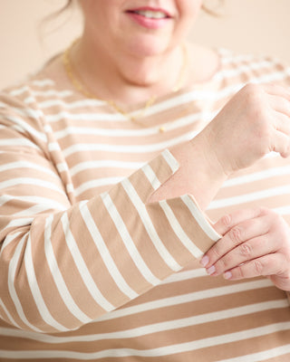 A close-up of a woman wearing a beige and white striped long-sleeve top, adjusting the cuff of the sleeve. This is the Wellfleet Breton T-Shirt sewing pattern from Cashmerette.