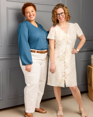 Two women standing against a gray paneled wall, one in a blue top and white pants, the other in a white dress. This is the Inman Top & Dress sewing pattern from Cashmerette.