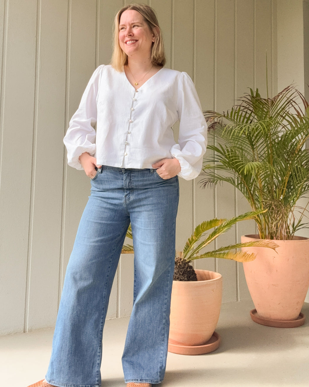 Woman wearing a white blouse and blue jeans standing in front of potted plants. This is the Inman Top & Dress sewing pattern from Cashmerette.