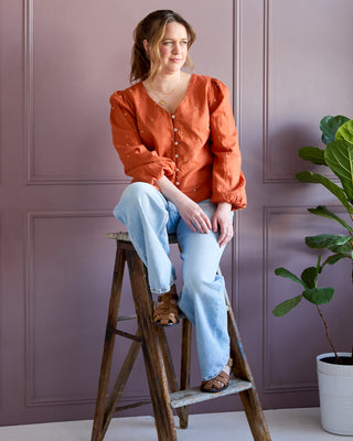 Woman sitting on a wooden stool against a purple wall with a plant to the side. This is the Inman Top & Dress sewing pattern from Cashmerette.