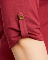 Close-up of a red shirt with a button on a blurred background. This t-shirt is the Concord T-Shirt sewing pattern from Cashmerette.