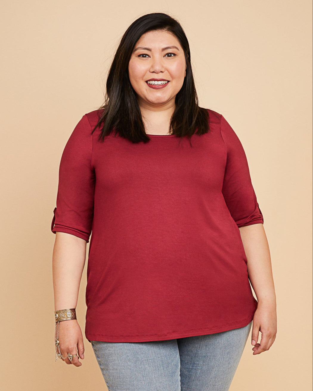 Woman wearing a red top and blue jeans on a beige background. This t-shirt is the Concord T-Shirt sewing pattern from Cashmerette.