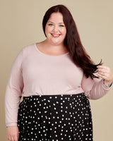 Woman wearing a light pink top and black polka dot pants against a beige background. This t-shirt is the Concord T-Shirt sewing pattern from Cashmerette.